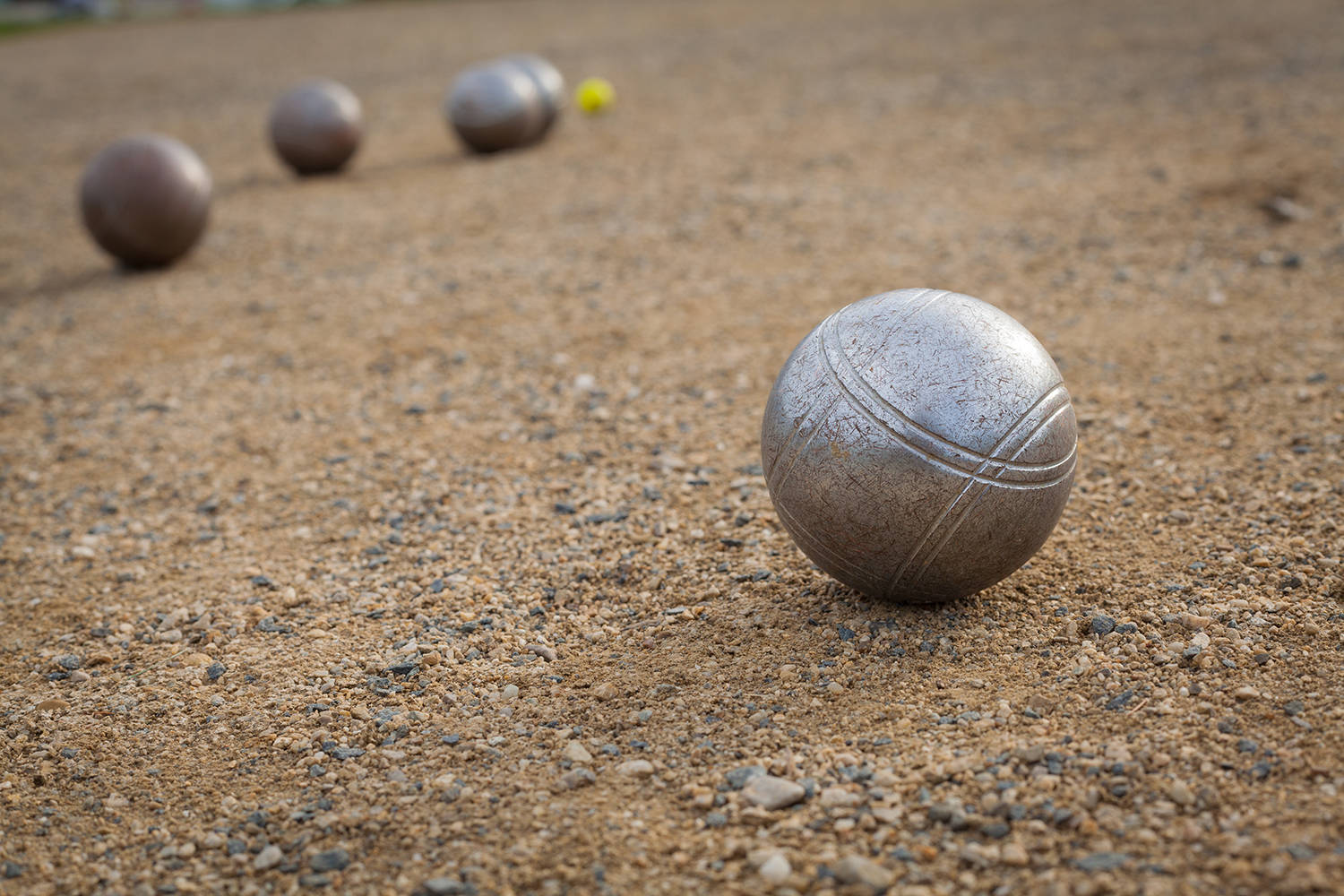 Petanque balls on a sandy pitch with other metal ball in the bac