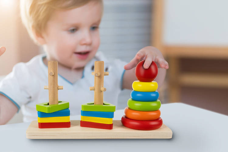 child little boy playing wooden toy pyramid himself at home or kindergarten. early development of children